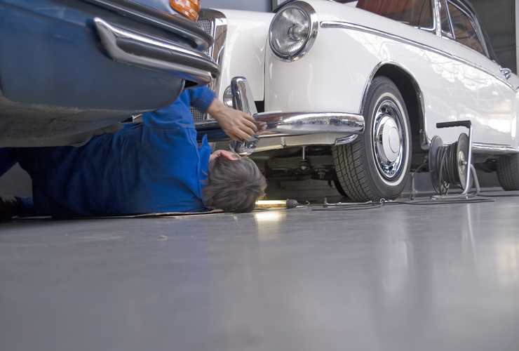 Car mechanic lies between two old timer cars.